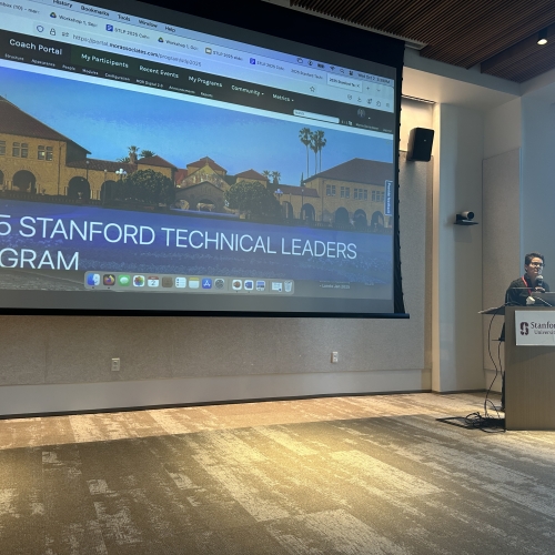 A wall sized screen in a conference room showing the home page of the Stanford Technical Leadership Program portal