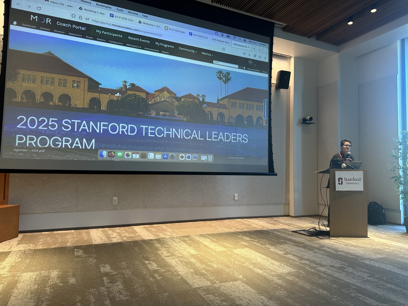 A wall sized screen in a conference room showing the home page of the Stanford Technical Leadership Program portal